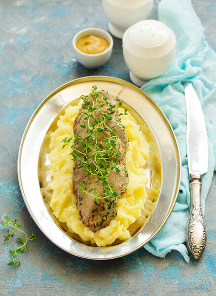 Baked pork tenderloin in herbs, with mashed potatoes and garnish.