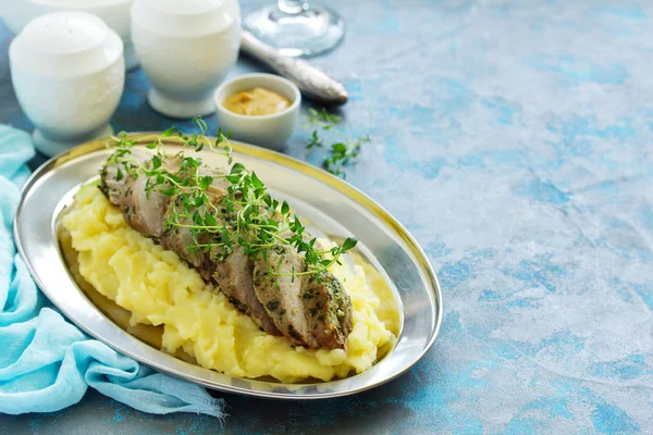 Baked pork tenderloin in herbs, with mashed potatoes and garnish.