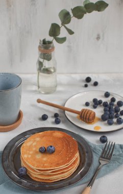 Kahvaltı sahne konseptiyle krep, yaban mersini ve bal bal kaşığı, vazo ile okaliptüs arka planda üzerinde