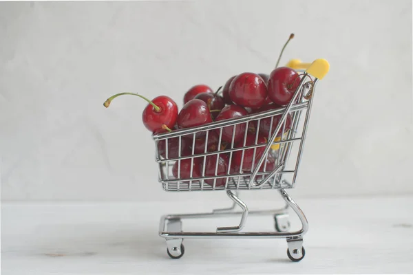Summer shopping or healthy eating concept, fresh cherries in small shopping cart on white background, copy space