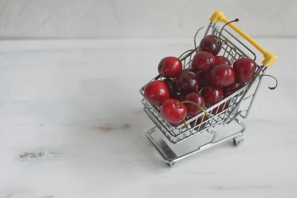 Summer shopping or healthy eating concept, fresh cherries in small shopping cart on white background, copy space