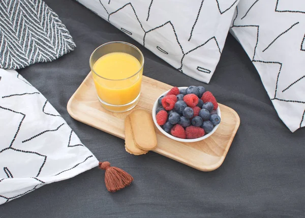 Breakfast bed Wooden tray Hotel room Early morning Concept interior Copy space Geometric sheet and pillow case Berries Orange juice Biscuits