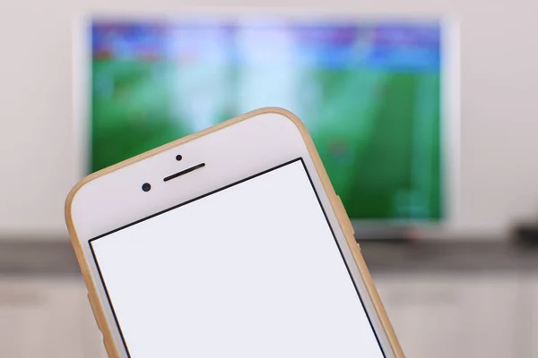 Football fan Sharing game result concept Smartphone with blank white screen with football game on tv on the background Gambling concept