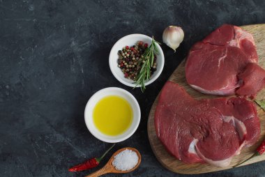 Taze çiğ et sığır eti biftek zeytinyağı baharat sıcak tuz ahşap kaşık biber biberiye sarımsak yemek kavramı yemek kavramı koyu beton arka üst düz koymak kopya alanı göster