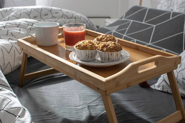 Christmas morning, Valentines day, cozy morning, hotel room - breakfast in bed, wooden tray with coffee, muffins, apple, orange juice on the bed. Modern scandinavian bedroom interior.