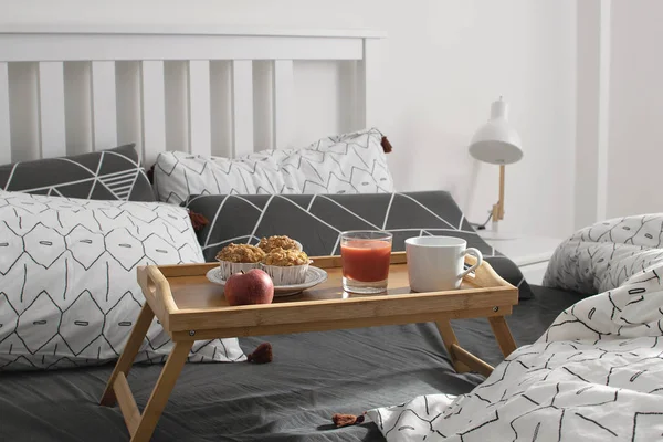 Christmas morning, Valentines day, cozy morning, hotel room - breakfast in bed, wooden tray with coffee, muffins, apple, orange juice on the bed. Modern scandinavian bedroom interior.