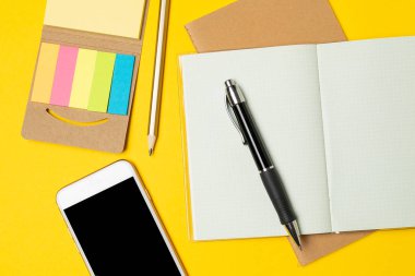 İş, planlama kavramı - iş yerinde, not defteri, yapışkan notlar, akıllı telefon ve kalem üzerinde parlak sarı arka plan, düz yatıyordu