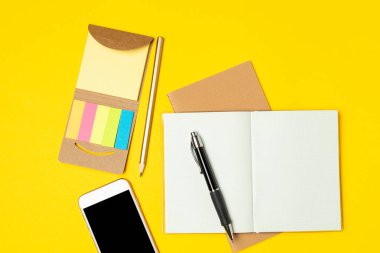 İş, planlama kavramı - iş yerinde, not defteri, yapışkan notlar, akıllı telefon ve kalem üzerinde parlak sarı arka plan, düz yatıyordu