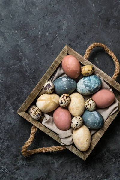 Spring easter minimal rustic style composition - organic naturally dyed easter eggs, qual eggs, curcuma, beetroot, hibiscus tea pigments in wooden tray, gray background, low key photo, copy space,