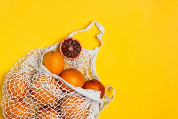 Naranjas sangrientas orgánicas en bolsa reutilizable de malla de algodón, respaldo amarillo — Foto de Stock