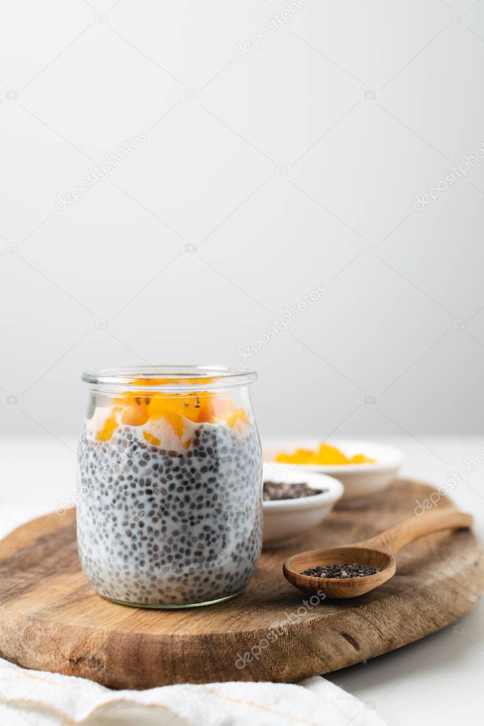 Chia pudding in glass jar with almond milk and mango on white ba