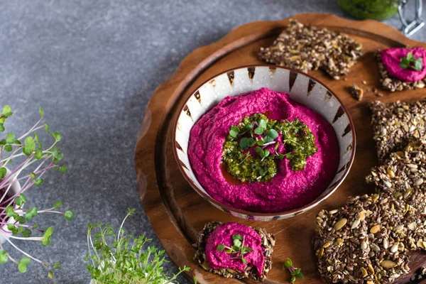 Roasted beet hummus in ceramic bowl, flax seed crackers on woode