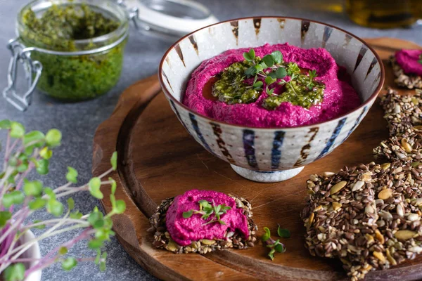 Roasted beet hummus in ceramic bowl, flax seed crackers on woode