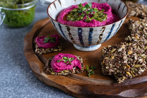 Roasted beet hummus in ceramic bowl, flax seed crackers on woode