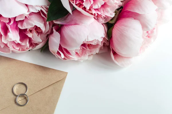 Anéis de casamento, envelope, flores de peônias no fundo branco, co — Fotografia de Stock