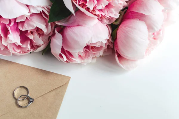 Anéis de casamento, envelope, flores de peônias no fundo branco, co — Fotografia de Stock