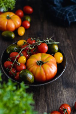 Koyu ahşap arka plan üzerinde bir kapta renkli organik domates
