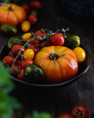 Koyu ahşap arka plan üzerinde bir kapta renkli organik domates