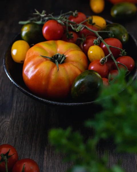 Koyu ahşap arka plan üzerinde bir kapta renkli organik domates