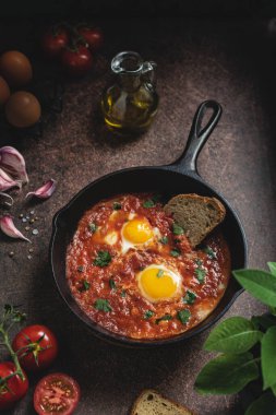 Shakshuka dökme demir tavada, baharatlı domates soslu orta doğu sahanda yumurta, üst manzara, koyu arkaplan