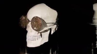 Kafatası elmas kaplı güneş gözlüğü takıyor. Siyaha doğru dönüyor ve daha fazla bozulma var.