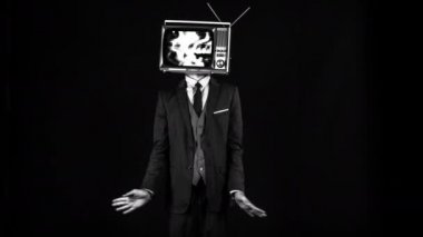 Bay Televizyon Şefi. Takım elbiseli havalı bir adam kafasında televizyonla dans ediyor. Televizyon parazitli ve gürültülü.