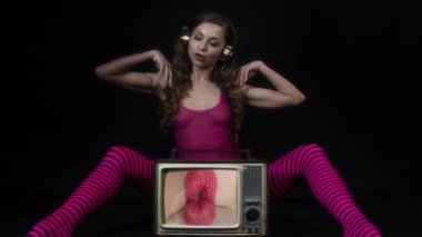 Çekici seksi disko kadın pembe vücutlu ve taytlı klasik televizyonla oturmuş kadın dudaklarını gösteriyor.