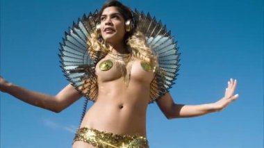 Güneşli bir arkaplanda dans eden, altın renkli kostümlü seksi bebek.