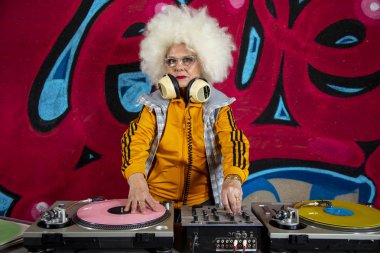 Graffiti duvarının önünde plakla müzik çalan şık bir büyükanne. 