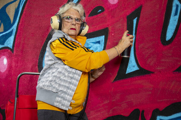 cool rebel grandmother painting graffiti against an urban wall