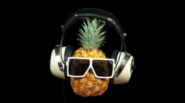 Siyah arka plan üzerinde güneş gözlüğü ve kulaklık ananas
