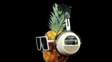 Siyah arka plan üzerinde güneş gözlüğü ve kulaklık ananas