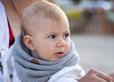 Annesiyle oturan, eşarplı, sevimli, küçük bir kız bebek.