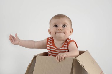 Çizgili elbiseli neşeli kız, karton kutuda oturuyor. 