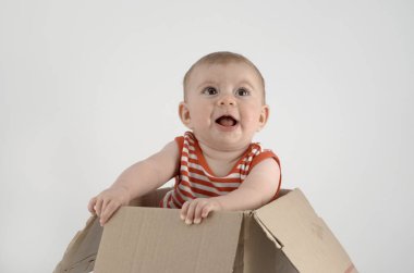 Çizgili elbiseli neşeli kız, karton kutuda oturuyor. 