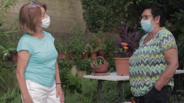 Twee volwassen vrouwen dragen beschermende gezichtsmaskers chatten — Stockvideo