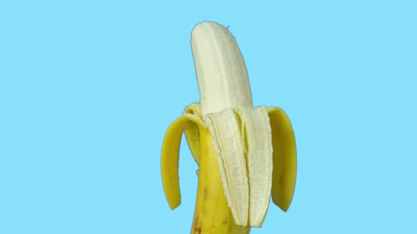 Imágenes animadas de un plátano medio pelado girando contra fondo azul — Vídeo de stock