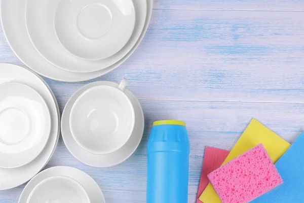 Cleaning powder and washcloths with white plates and cups on a blue wooden background