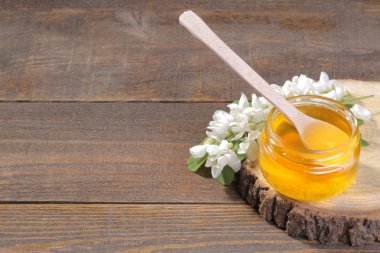 Bir kavanoz bal bal ve ahşap bir kaide üzerinde bir akasya dalı için tahta kaşıkla. Kahverengi zemin