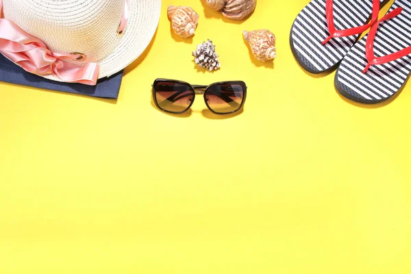 Beach accessories. Summer hat with flip-flops, sunny black glasses and seashells on a bright yellow background. Top view