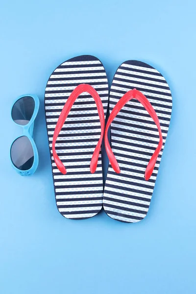 Mavi bir arka plan üzerinde mavi bir güneş gözlüğü ile parmak arası terlik. Üstten görünüm. Plaj aksesuarları