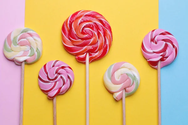 Multicolored round lollipops on a stick on colored bright backgrounds. Top view