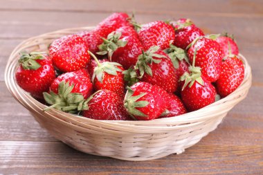 Bir sürü kahverengi ahşap arka plan üzerinde bir hasır sepet içinde olgun çilek