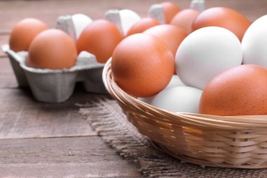 Bir hasır sepet yumurta tepsi kahverengi ahşap arka plan üzerinde yanında kahverengi ve beyaz tavuk yumurta.