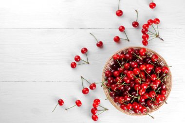 Bir sürü beyaz ahşap zemin üzerinde bir hasır sepet içinde rendelenmiş Olgun, kırmızı, taze kiraz. üstten görünüm