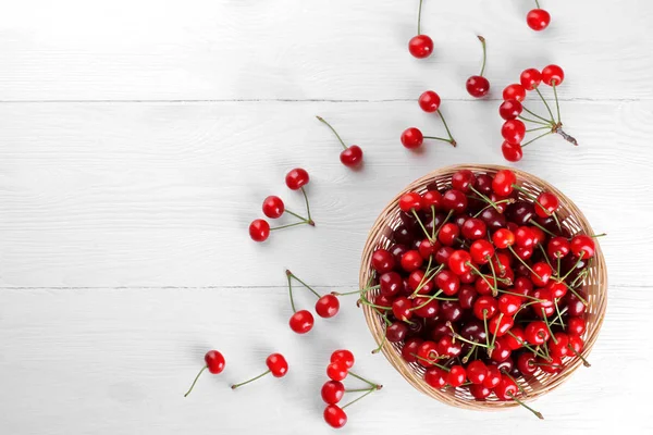 Bir sürü beyaz ahşap zemin üzerinde bir hasır sepet içinde rendelenmiş Olgun, kırmızı, taze kiraz. üstten görünüm