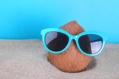 Deniz mavi bir arka plan üzerinde kum içinde güneş gözlüğü Hindistan cevizi