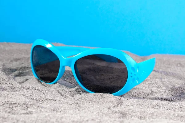 太阳镜蓝色在海的沙子在明亮的蓝色背景 — 图库照片