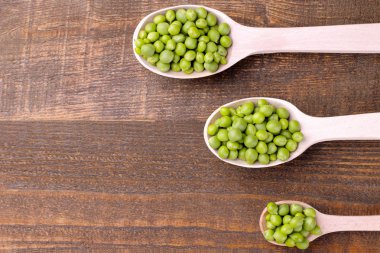 Kahverengi ahşap arka plan üzerinde bir tahta kaşık taze yeşil bezelye. Yazıt ile yer