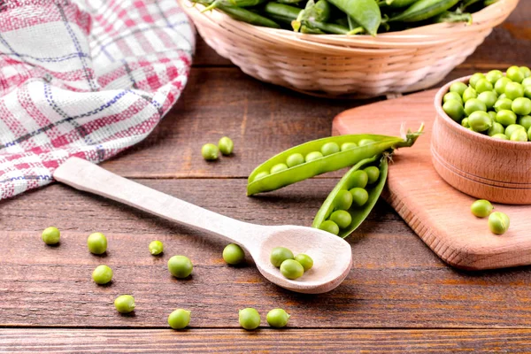 Fresh green peas in a wooden spoon next to peas in a stitch on a brown wooden background